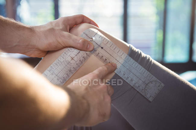 Immagine ritagliata del terapeuta maschile che misura il ginocchio del paziente femminile con goniometro in clinica — Foto stock