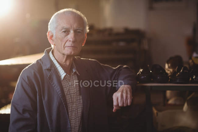 Старший улыбающийся сапожник, стоящий в мастерской — стоковое фото