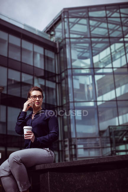 Бизнесмен разговаривает по мобильному телефону с офисным зданием — стоковое фото