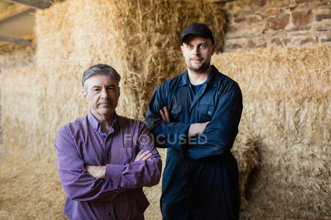 Retrato de agricultor e veterinário contra fardos de feno no celeiro — Fotografia de Stock