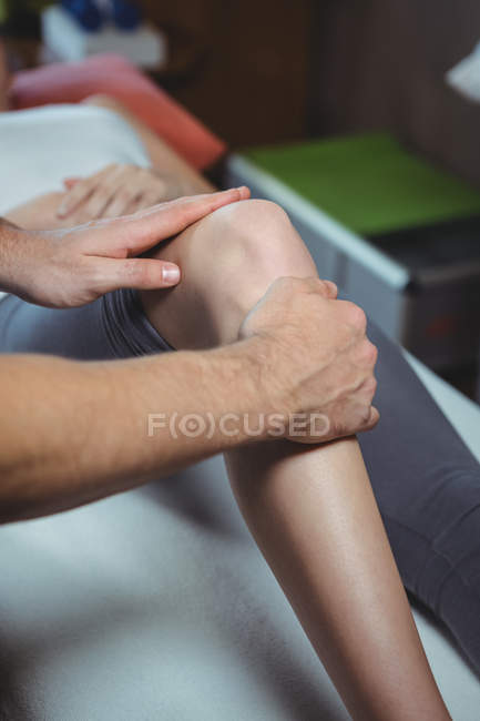 Imagen recortada del fisioterapeuta que da fisioterapia a la rodilla de una paciente femenina en la clínica - foto de stock