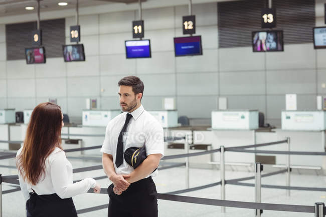 Piloto y auxiliar de vuelo interactuando entre sí en la terminal del aeropuerto - foto de stock