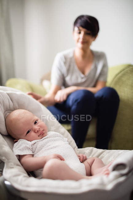 Baby lying in stroller while mother sitting on sofa on background at home — Stock Photo