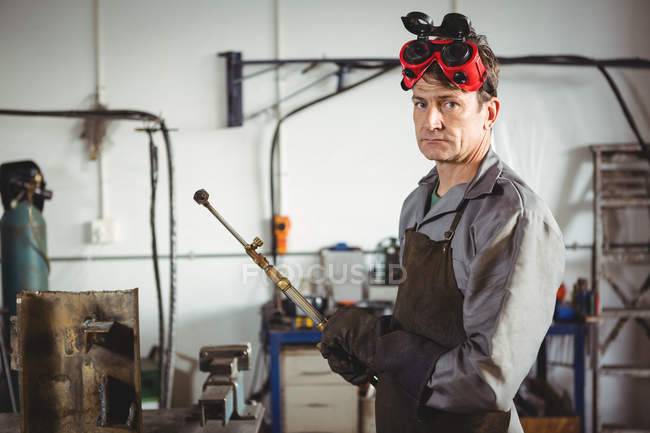 Portrait of welder standing with welding machine in workshop — Stock Photo