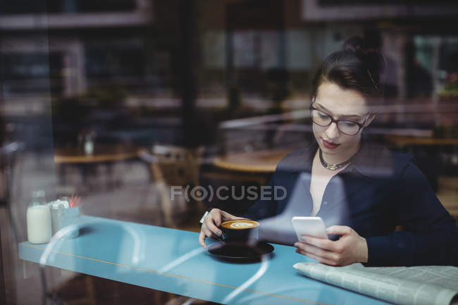 Молода жінка використовує мобільний телефон у кафе, який видно через скло — стокове фото