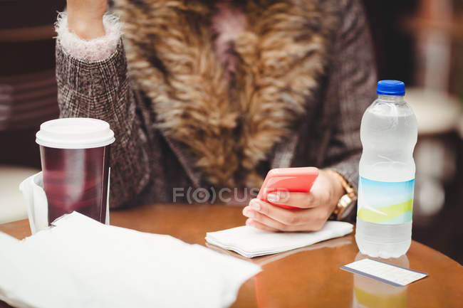 Midsection женщины, использующей смартфон, сидя в ресторане — стоковое фото
