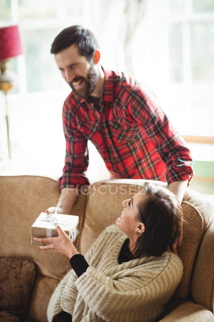 Man surprising woman with gift in living room at home — Stock Photo