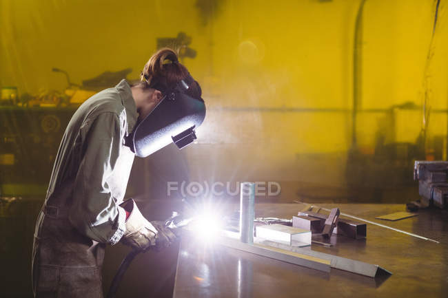 Soldadora femenina trabajando en pieza de metal en taller - foto de stock