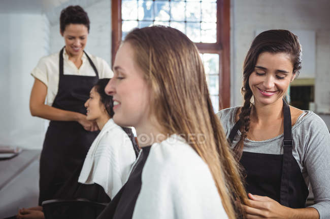 Улыбающиеся парикмахеры, работающие с клиентами в парикмахерской — стоковое фото