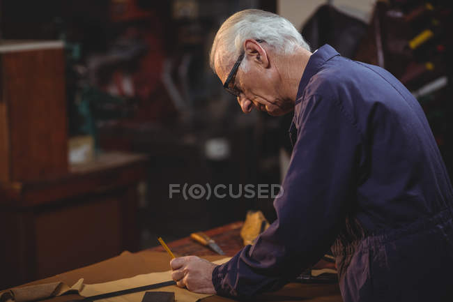 Обувщик режет кусок кожи в мастерской — стоковое фото