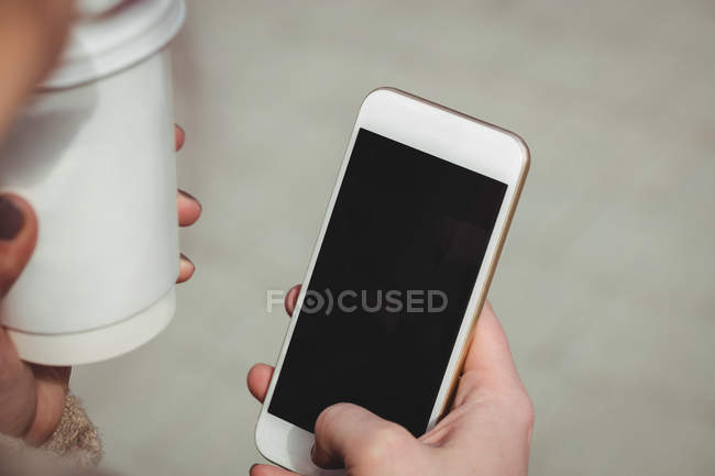 Обрезанное изображение женщины с мобильным телефоном и одноразовой чашкой — стоковое фото
