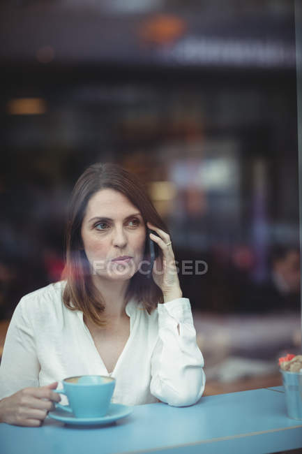 Femme tenant une tasse de café et parlant sur un téléphone portable à la cafétéria — Photo de stock