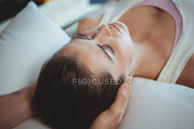 Fisioterapeuta masculino dando masaje en la cabeza a una paciente femenina en la clínica - foto de stock