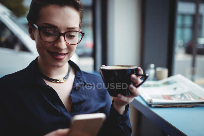 Mujer joven sonriente usando el teléfono móvil en la cafetería - foto de stock