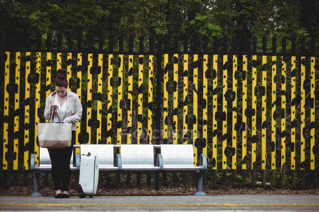 Молодая женщина стоит напротив забора на платформе железнодорожного вокзала — стоковое фото