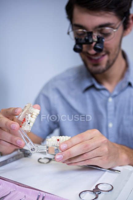 Dentiste masculin regardant le modèle de bouche avec des loupes dentaires — Photo de stock
