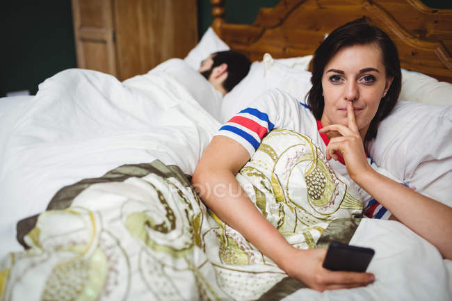 Жінка використовує мобільний телефон з пальцем на губах у спальні — стокове фото