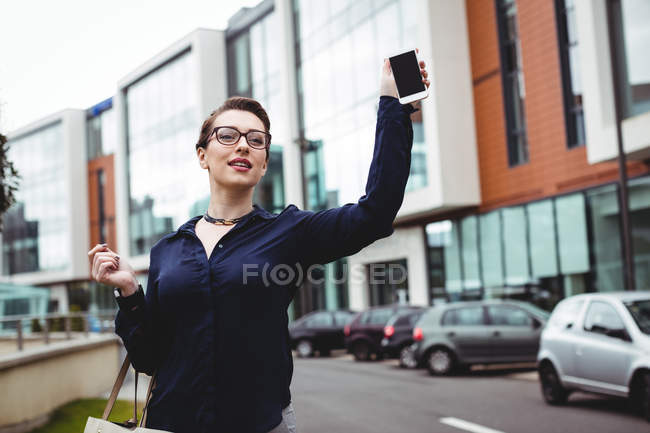 Деловая женщина держит мобильный телефон по зданиям на дороге — стоковое фото
