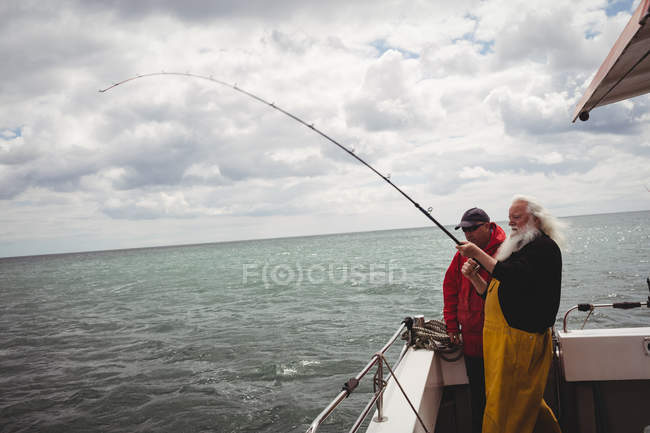 Dos pescadores pescando con caña de pescar desde el barco - foto de stock