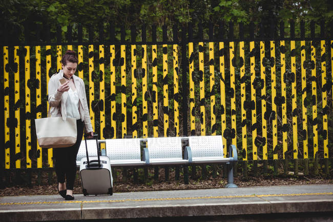 Longitud total de la mujer de pie contra la valla en la plataforma de la estación de ferrocarril - foto de stock
