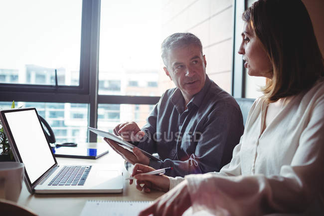 Mann und Frau diskutieren im Büro über digitales Tablet und Laptop — Stockfoto