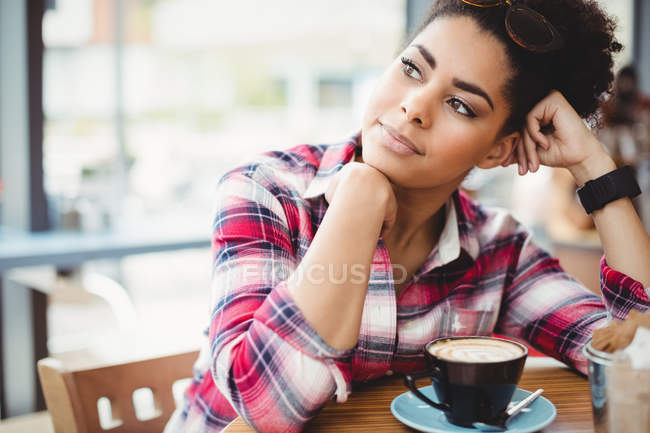 Mujer sonriente pensativa sentada a la mesa en el restaurante - foto de stock