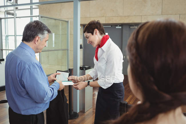 Empresario mostrando su tarjeta de embarque en el mostrador de facturación en el aeropuerto - foto de stock