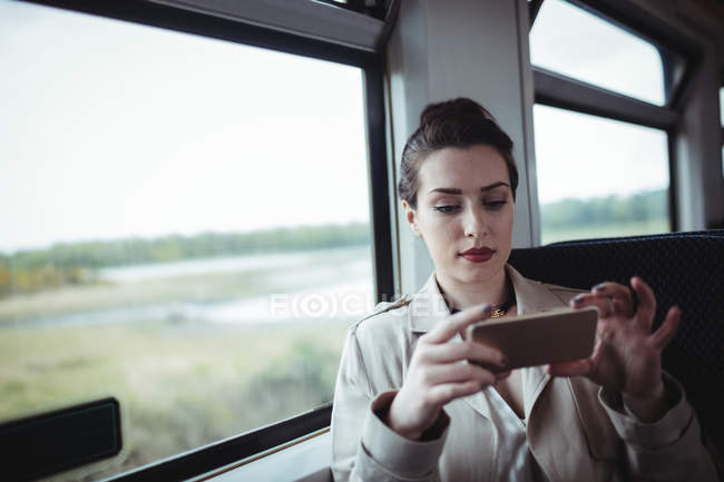 Bella donna che utilizza il cellulare mentre seduto in treno — Foto stock