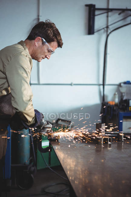 Handsome welder cutting metal with electric tool in workshop — Stock Photo