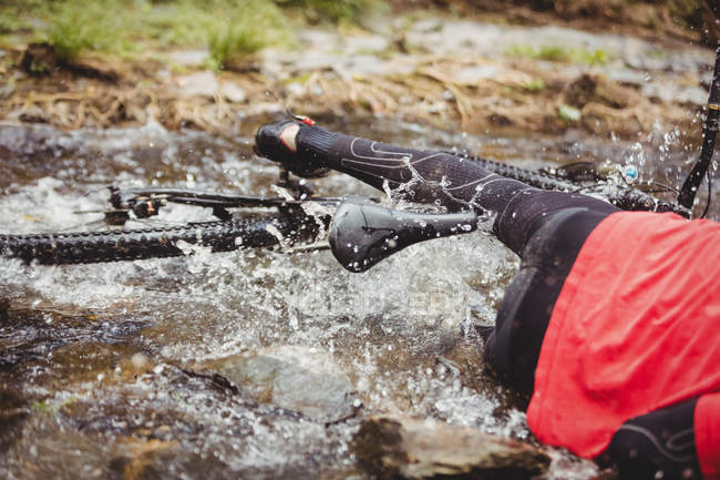 Low section of mountain biker fallen in stream at forest — Stock Photo