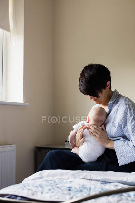 Madre sentada con su bebé en el dormitorio en casa - foto de stock