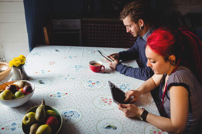Молода пара хіпстерів використовує таблетки, сидячи за столом вдома — стокове фото