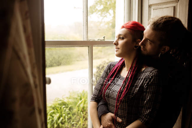 Романтическая молодая пара обнимается, глядя в окно дома — стоковое фото
