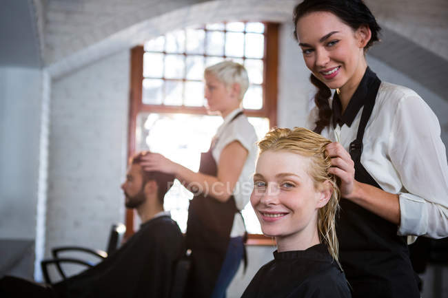 Портрет усміхненого стиліста для волосся, що масажує волосся клієнта в салоні — стокове фото
