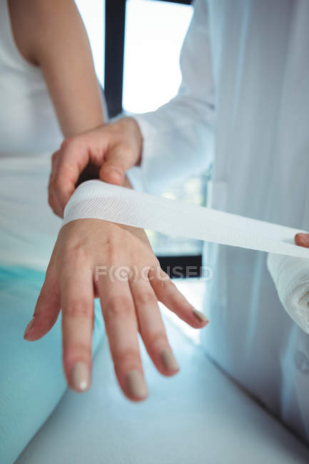 Imagen recortada del terapeuta masculino poniendo vendaje en la mano del paciente femenino - foto de stock
