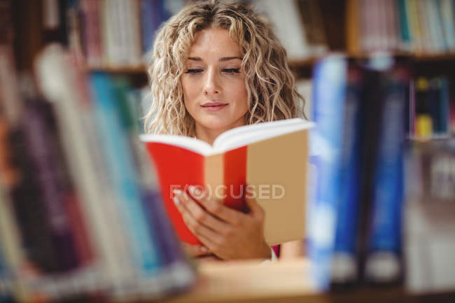 Schöne Frau liest Buch in Bibliothek — Stockfoto