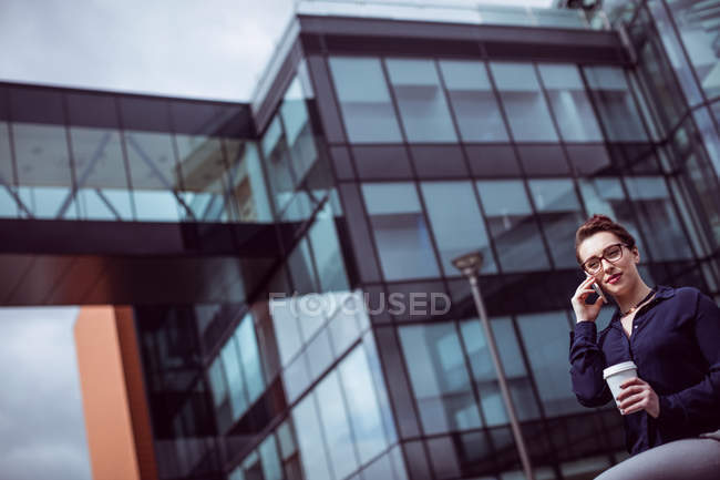 Young businesswoman talking on mobile phone against modern building — Stock Photo