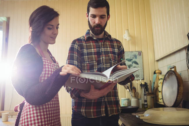 Пара глядя на книгу рецептов на кухне дома — стоковое фото