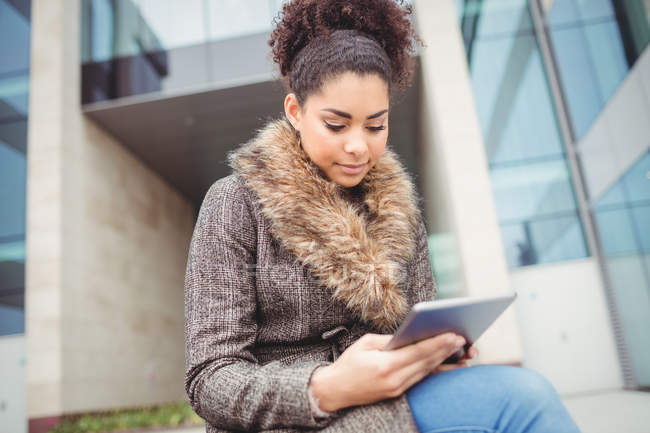 Young woman holding digital tablet while sitting against building — Stock Photo