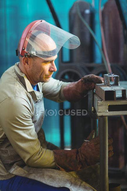 Saldatore maschio esaminando pezzo di metallo in officina — Foto stock
