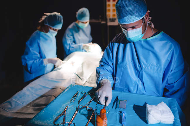 Хирург забирает ножницы из подноса во время операции — стоковое фото