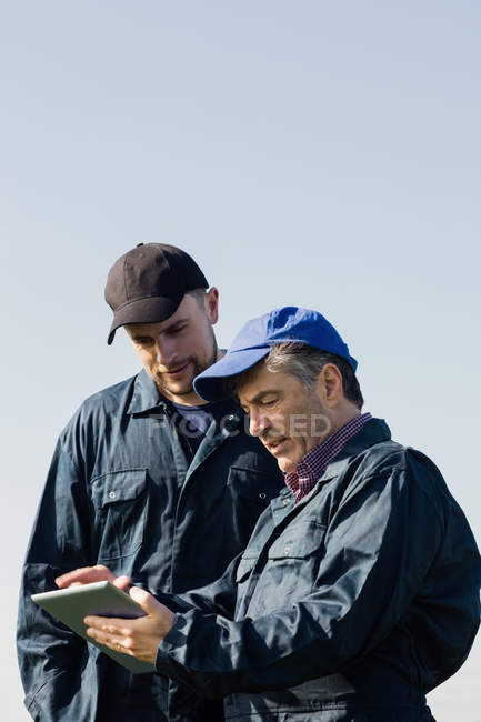Trabalhadores agrícolas discutindo sobre tablet computador contra céu limpo — Fotografia de Stock