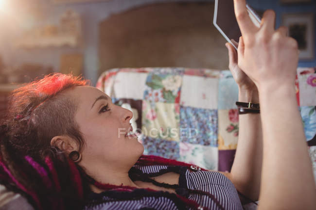 Joven mujer hipster usando tableta digital mientras se relaja en el sofá en casa - foto de stock