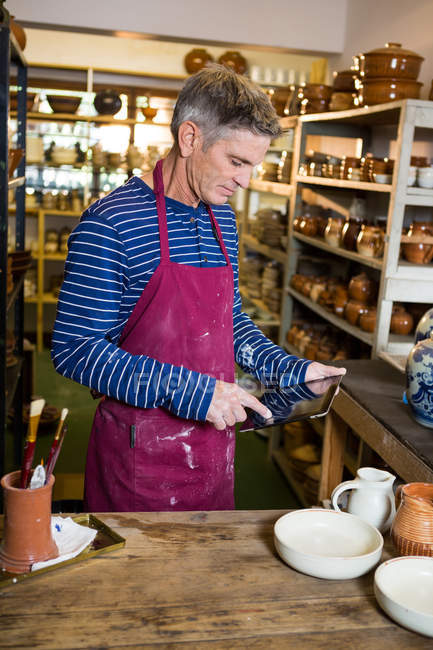 Мужчина гончар с помощью цифровой планшет в керамической мастерской — стоковое фото
