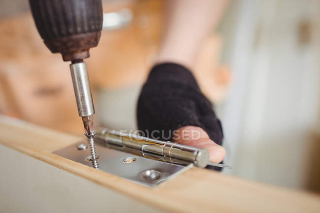 Abgeschnittenes Bild eines Zimmermanns, der zu Hause Schraube an Scharnier an Holztür schraubt — Stockfoto
