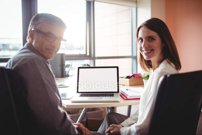Portrait of man and woman sitting at table in office — Stock Photo
