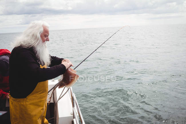 Вид сбоку на рыбака, ловящего рыбу с лодки — стоковое фото