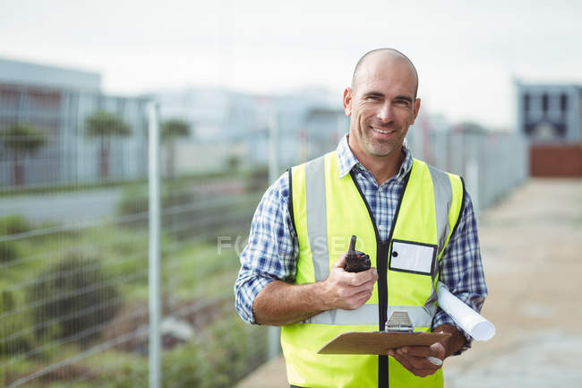 Construction worker holding walkie-talkie and clipboard outside office — Stock Photo