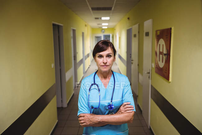 Porträt einer Krankenschwester, die mit verschränkten Armen im Krankenhausflur steht — Stockfoto
