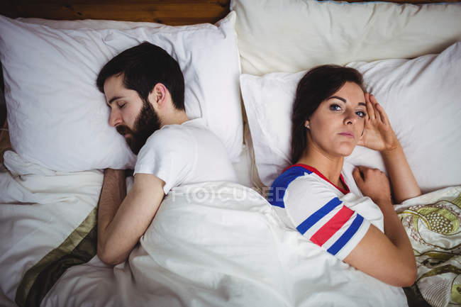 Jovem deitada na cama com o homem adormecido no quarto — Fotografia de Stock